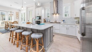 A modern kitchen with a central island, white cabinetry, stainless steel appliances, and a dining area with bar stools.