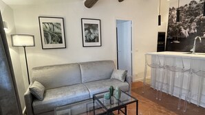 En stue med sofa, sofabord i glas og et køkkenområde med barstole.