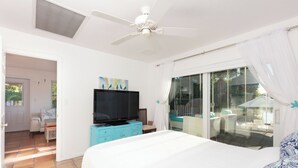 Una camera da letto con un letto, una televisione, una ventola a soffitto e una porta scorrevole in vetro che dà su un balcone.
