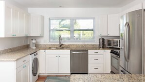 Una cucina moderna con mobili bianchi, elettrodomestici in acciaio inossidabile, forno integrato e una finestra con persiane.