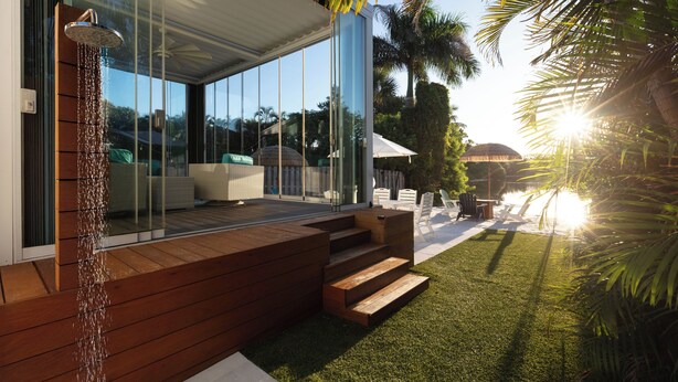 Una casa moderna con veranda vetrata, terrazza in legno e elemento d'acqua.