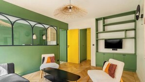 A modern living room with a sofa, armchair, and a coffee table. There is a television mounted on the wall and a door leading to another room.