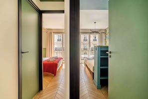 Et hotelværelse med fiskebensparket, en seng med rødt sengetæppe, en blå garderobe og en balkon med udsigt til bygninger.