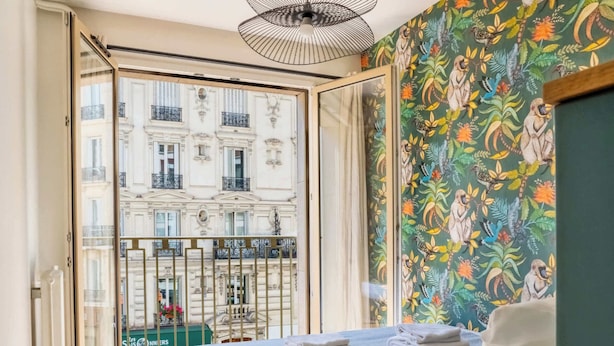 A bedroom with a bed, a view of a building through a glass door, and a patterned wall.