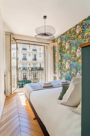 A bedroom with a bed, a view of a building through a glass door, and a patterned wall. - Stylish 3BD for 10 guests next to Invalides! (Paris)