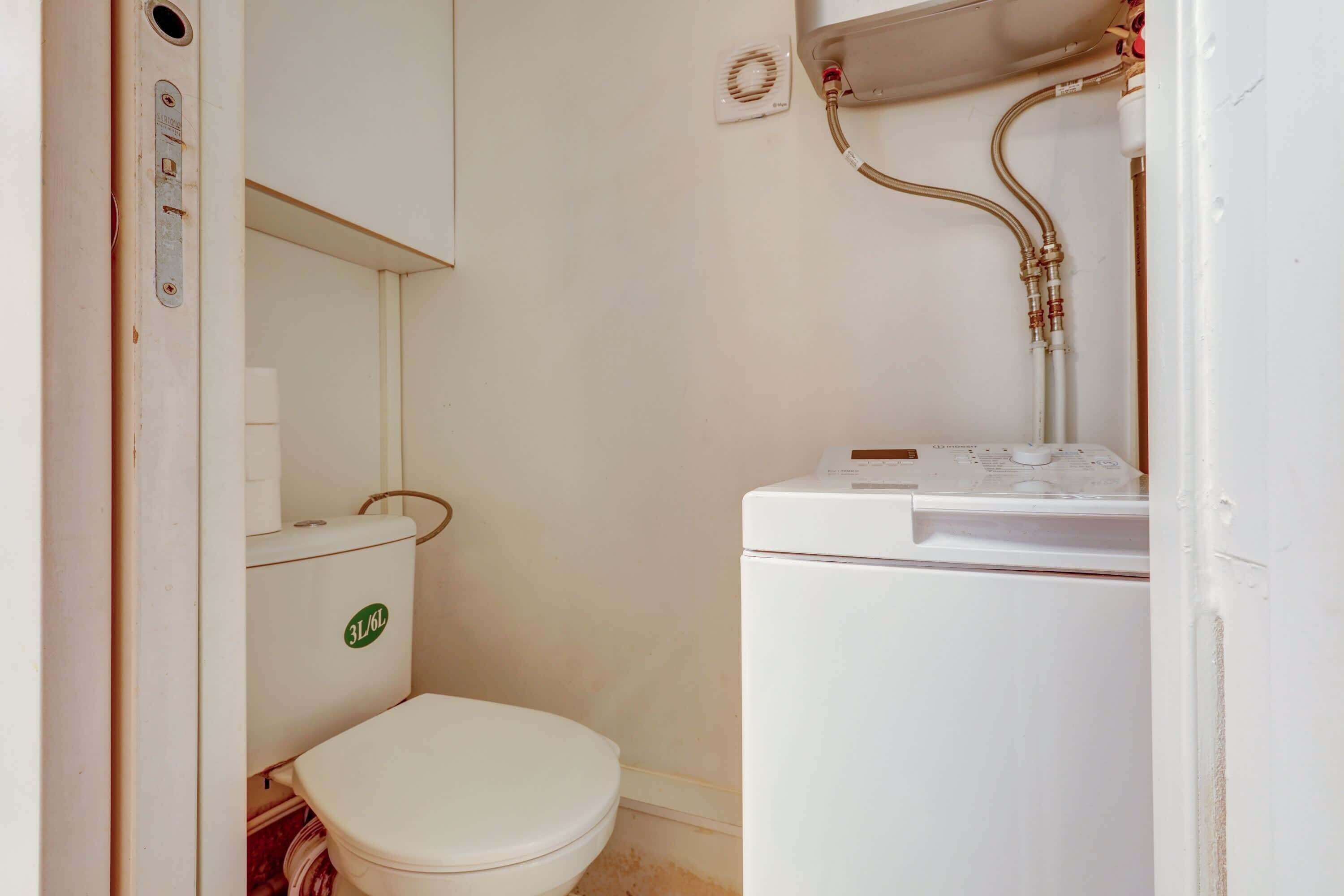 Une petite salle de bain comprenant des toilettes, un lave-linge et un petit lavabo.