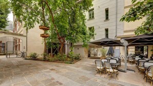 An outdoor seating area with stone flooring, a tree, and a restaurant sign. - 2 bedroom in the heart of Le Marais! (Paris)