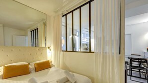 A hotel room with a large bed, two pillows, a neatly made bed, a mirror, a window with curtains, and a small table with chairs. - 2 bedroom in the heart of Le Marais! (Paris)