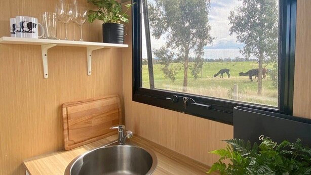 A compact kitchen with a stainless steel sink, wooden countertop, and a window offering a view of a rural landscape. - Maluridae Creek Views by Tiny Away (Lawrence)