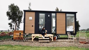 A modern, compact living space with a wooden exterior and large glass doors. - Maluridae Creek Views by Tiny Away (Lawrence)