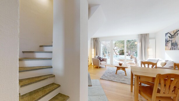 A modern interior with a staircase, a dining area, and a living room with a view of the outdoors.