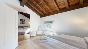 A bedroom with two beds, a window, and a wooden ceiling.
