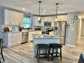 A modern kitchen with white cabinets, stainless steel appliances, a large island with stools, and pendant lighting.
