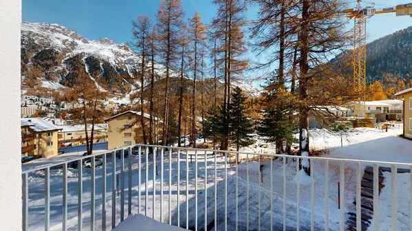 A snow-covered balcony with a view of a mountainous landscape, a residential area, and a construction crane in the background. - Renovated in 2020, 5½-room apartment on the 1st floor, distributed over two floo (Pontresina)