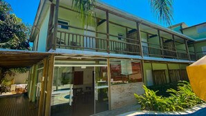A two-story building with a balcony, a swimming pool, and a wooden deck. - Pousada BeachCamp Maresias (São Sebastião)