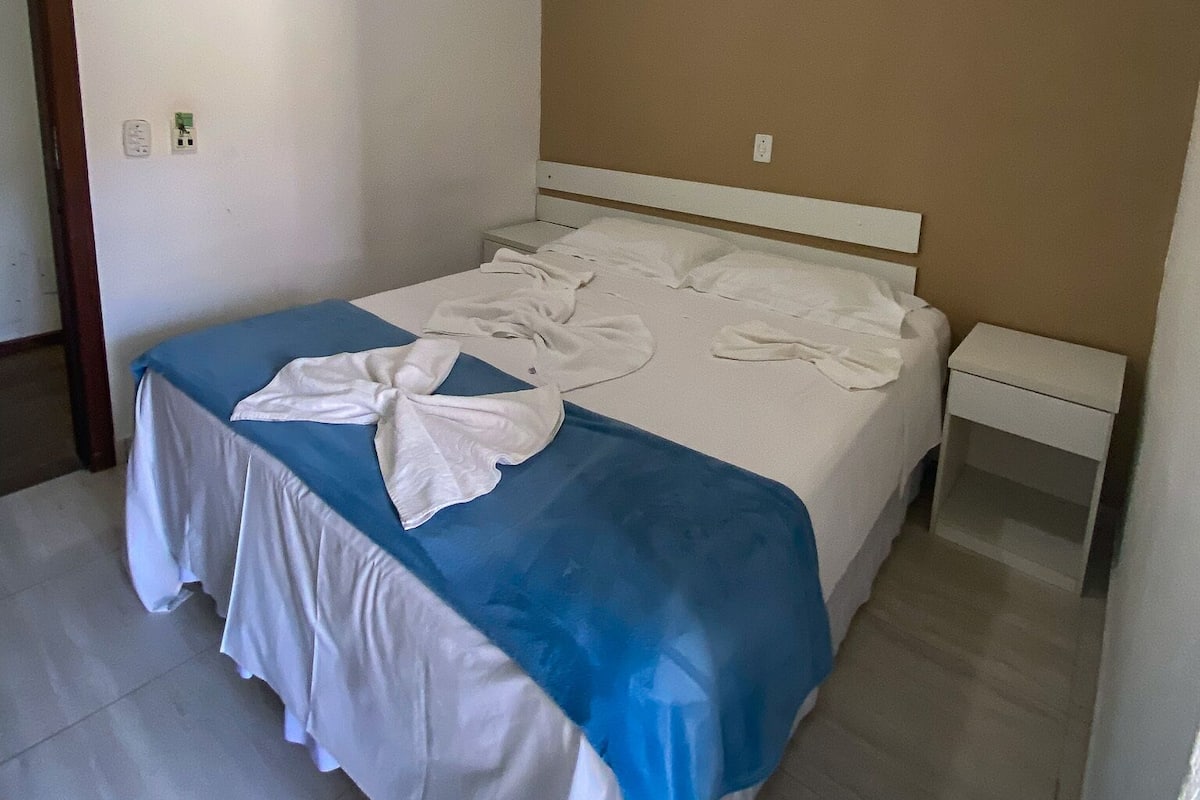 A hotel room with a bed, a ceiling fan, an air conditioning unit, and a nightstand.