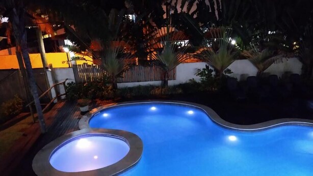 A swimming pool with a unique curved design, surrounded by a wooden deck and potted plants. - Pousada BeachCamp Maresias (São Sebastião)