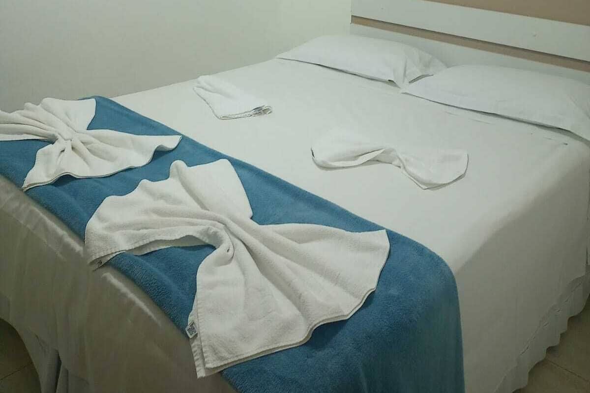 A single bed with white linens, a blue towel, and a white robe on the bed.