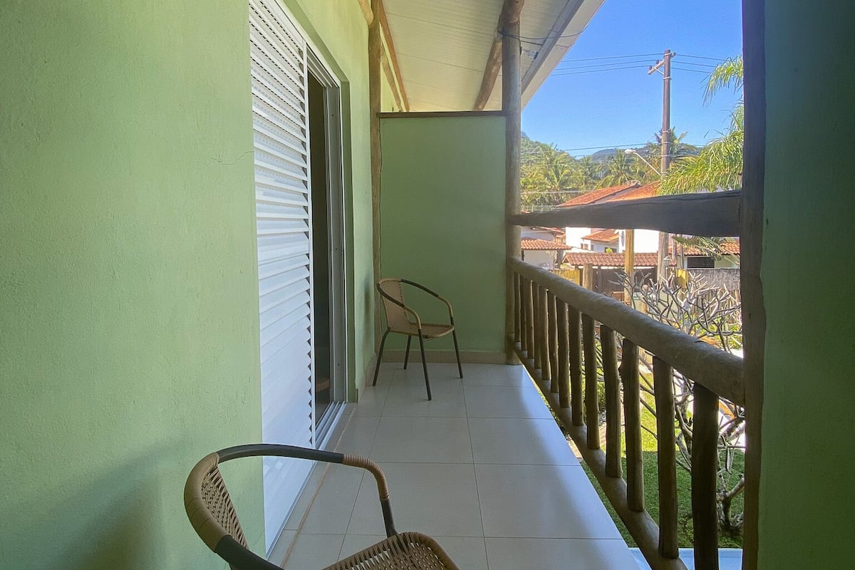 A balcony with a wicker chair, a small table, and a view of a residential area.