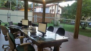 An outdoor office area with multiple computer desks and chairs, large windows, and a view of a residential area. - Pousada BeachCamp Maresias (São Sebastião)