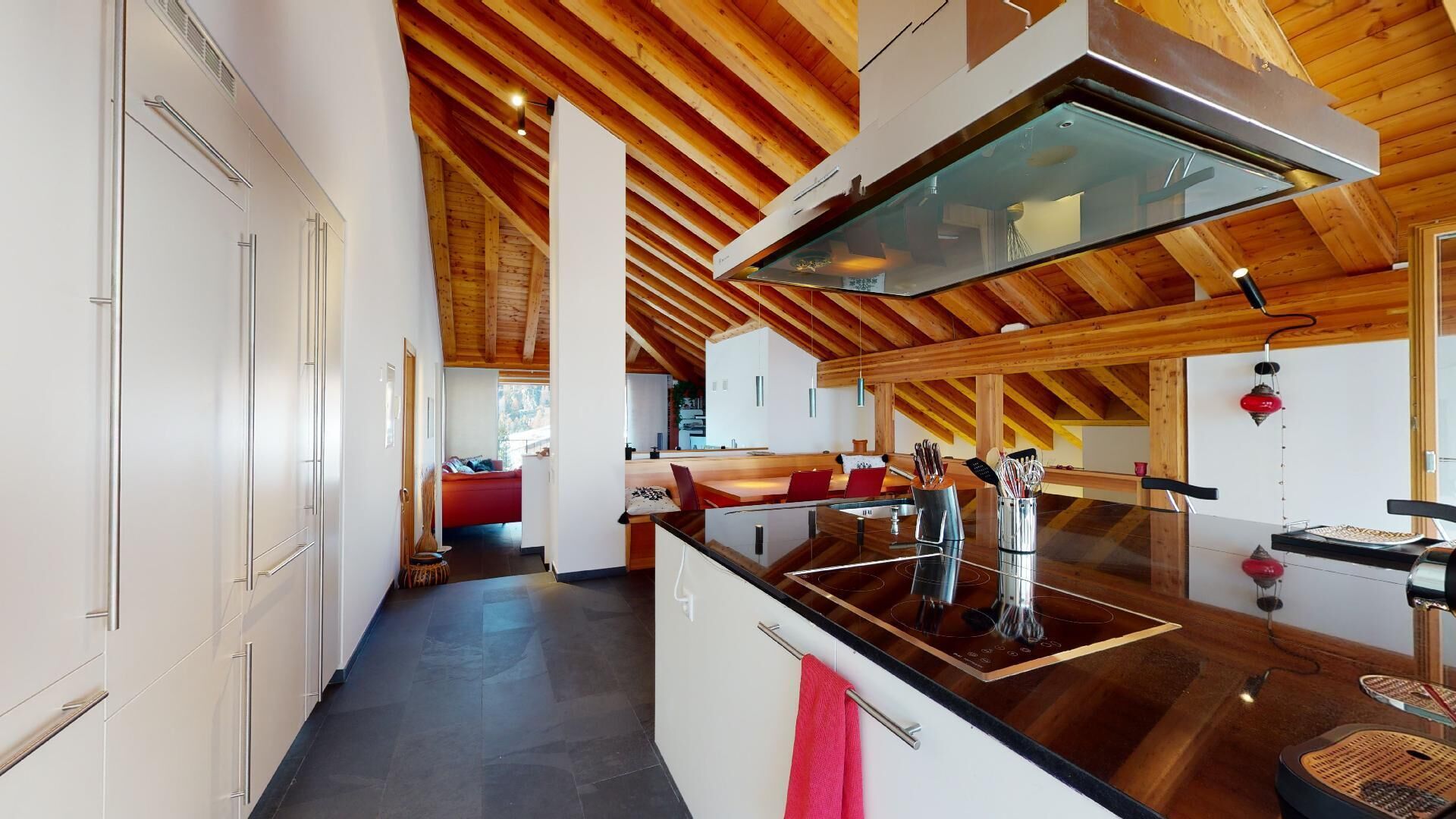 A modern kitchen with a central island, wooden ceiling beams, and a view to a dining area.