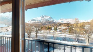 A view from a balcony with a snow-covered landscape, a mountain, and buildings in the background. - Large 3-½ room maisonette on the 2nd floor. (Silvaplana-Surlej)