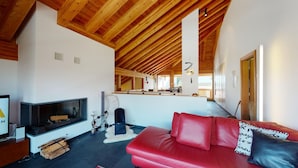 A modern living room with a fireplace, a red leather sofa, and wooden ceiling beams. - Large 3-½ room maisonette on the 2nd floor. (Silvaplana-Surlej)