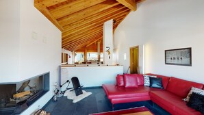 A modern living room with a red leather sofa, a fireplace, and a wooden ceiling. - Large 3-½ room maisonette on the 2nd floor. (Silvaplana-Surlej)