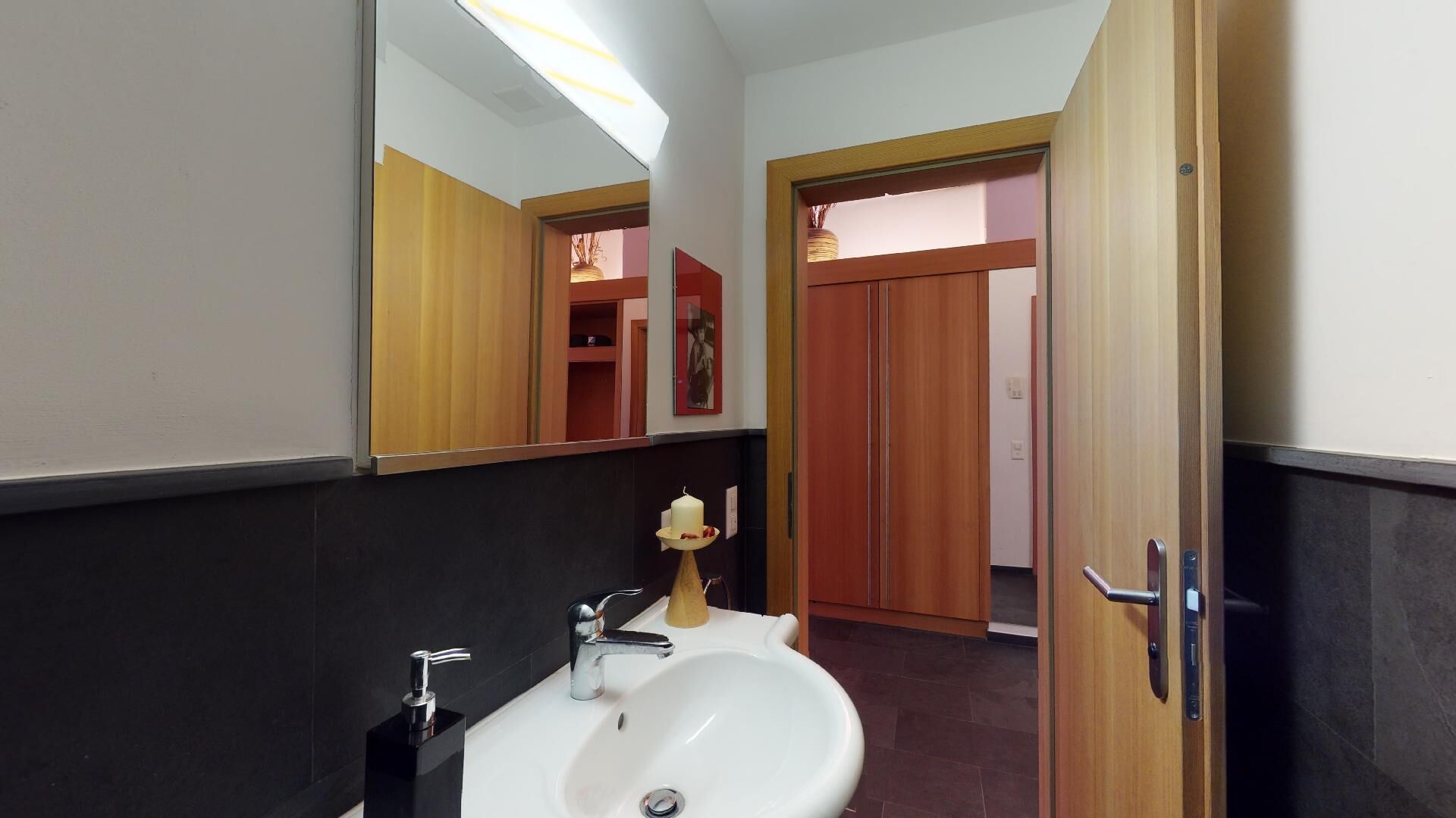 Une salle de bain avec un lavabo blanc, un miroir et une porte en bois.
