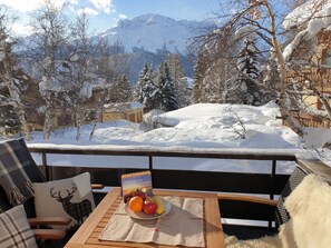 A balcony with a table set for breakfast, overlooking a snowy mountain landscape.