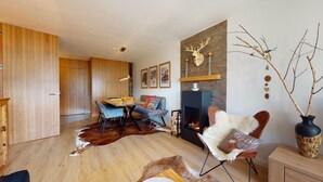 A modern living room with a fireplace, wooden flooring, a dining area, and a sofa. - 3-room apartment on the first floor, 67m2. (Celerina/Schlarigna)