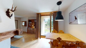 Ein gemütliches Interieur mit einem Holzesstisch, einem Bücherregal und einem großen Fenster mit Blick ins Freie.