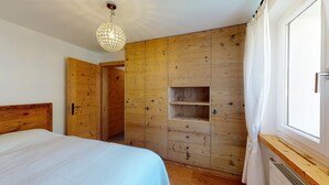 A bedroom with a wooden wardrobe, a bed, and a hanging light fixture. - 2-room apartment on the 1st floor. (Celerina/Schlarigna)
