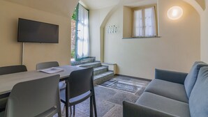 Une pièce comprenant une table à manger, des chaises, un canapé, un téléviseur, une fenêtre avec des rideaux et un escalier menant à un niveau supérieur.