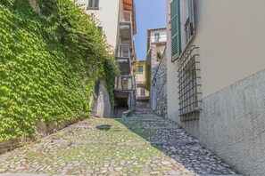 A narrow cobblestone alley with stone buildings on either side, featuring balconies and a staircase leading up.