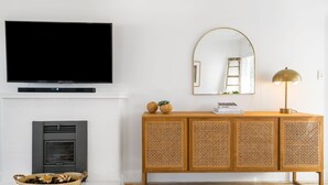 Ein Wohnzimmer mit Flachbildfernseher über einem Kamin, einem Holztischchen mit Dekoration und einem Spiegel mit gebogenem Rahmen.