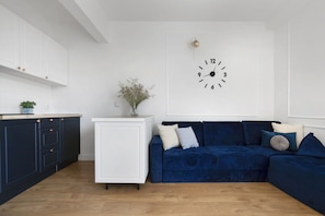 Cozy living space with a minimalist design, featuring a white cabinet, a sectional sofa, and a large wall clock.