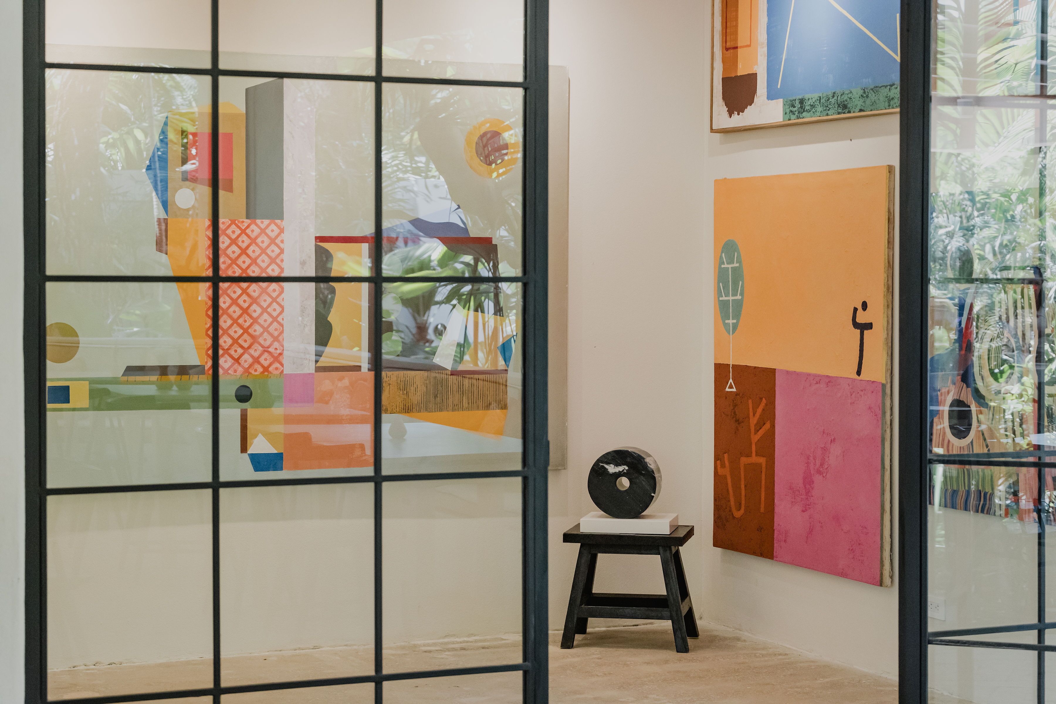 Uma galeria de arte com pinturas abstratas e uma escultura em exposição.