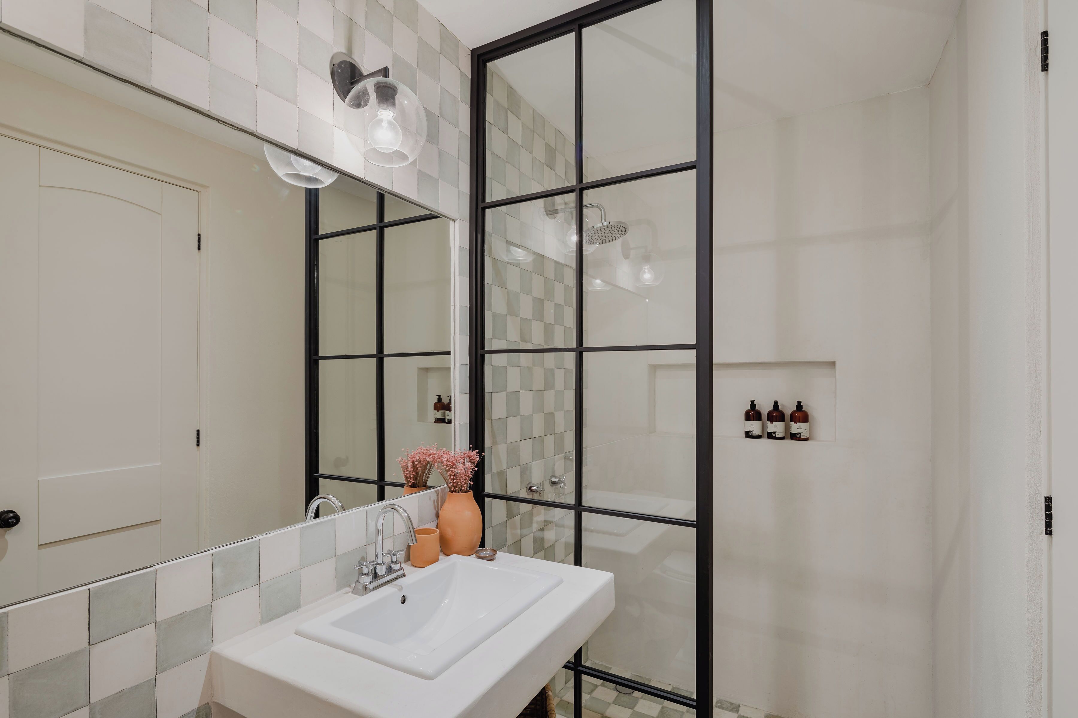 Casa de banho com lavatório branco, espelho e cabine de duche em vidro.