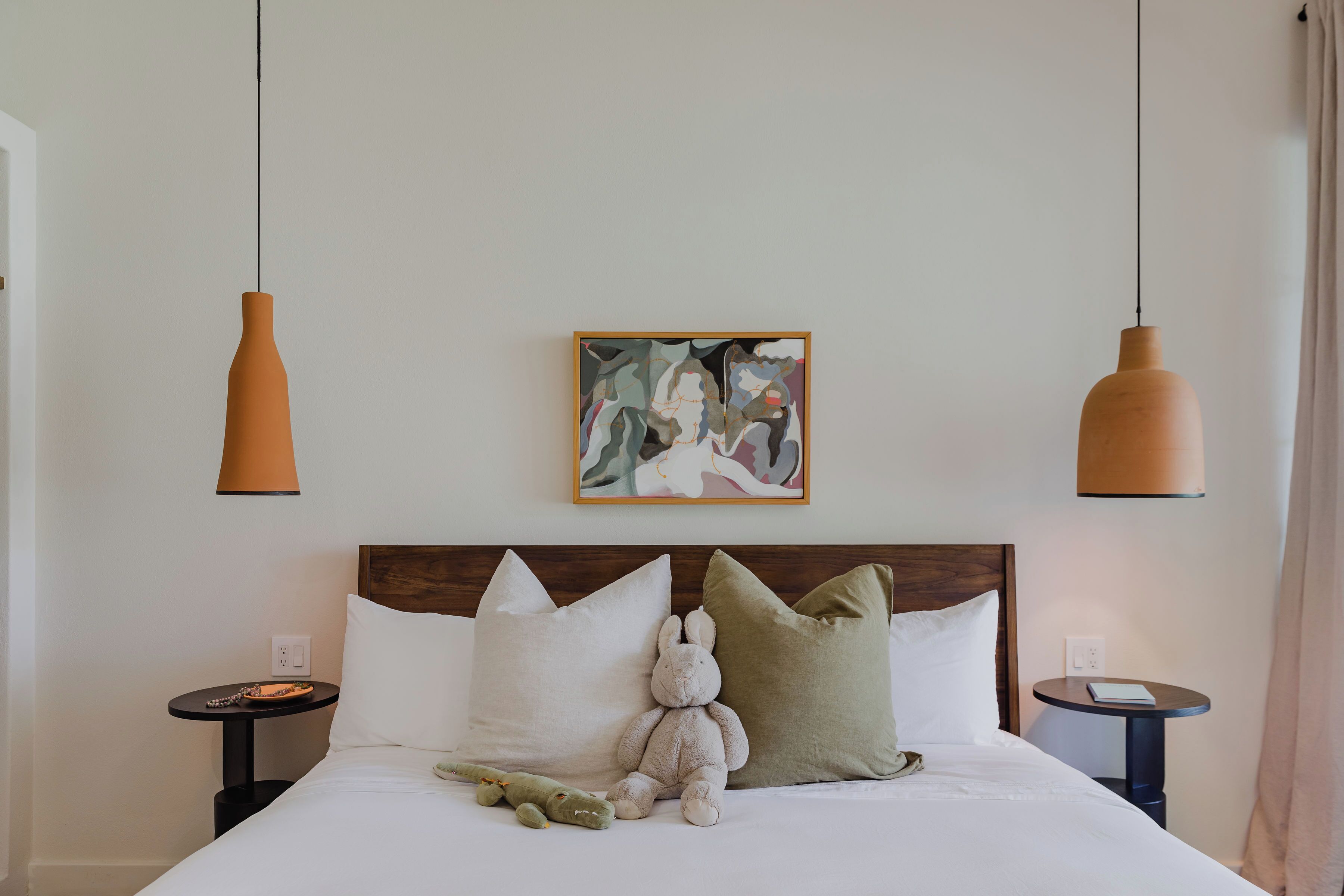 A neatly made bed with pillows, a plush toy, and a framed artwork above it.