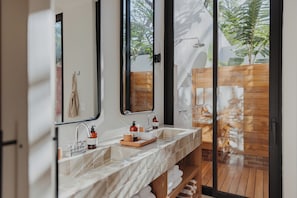 A modern bathroom with a large mirror, two sinks, a shower, and a view of the outdoors.