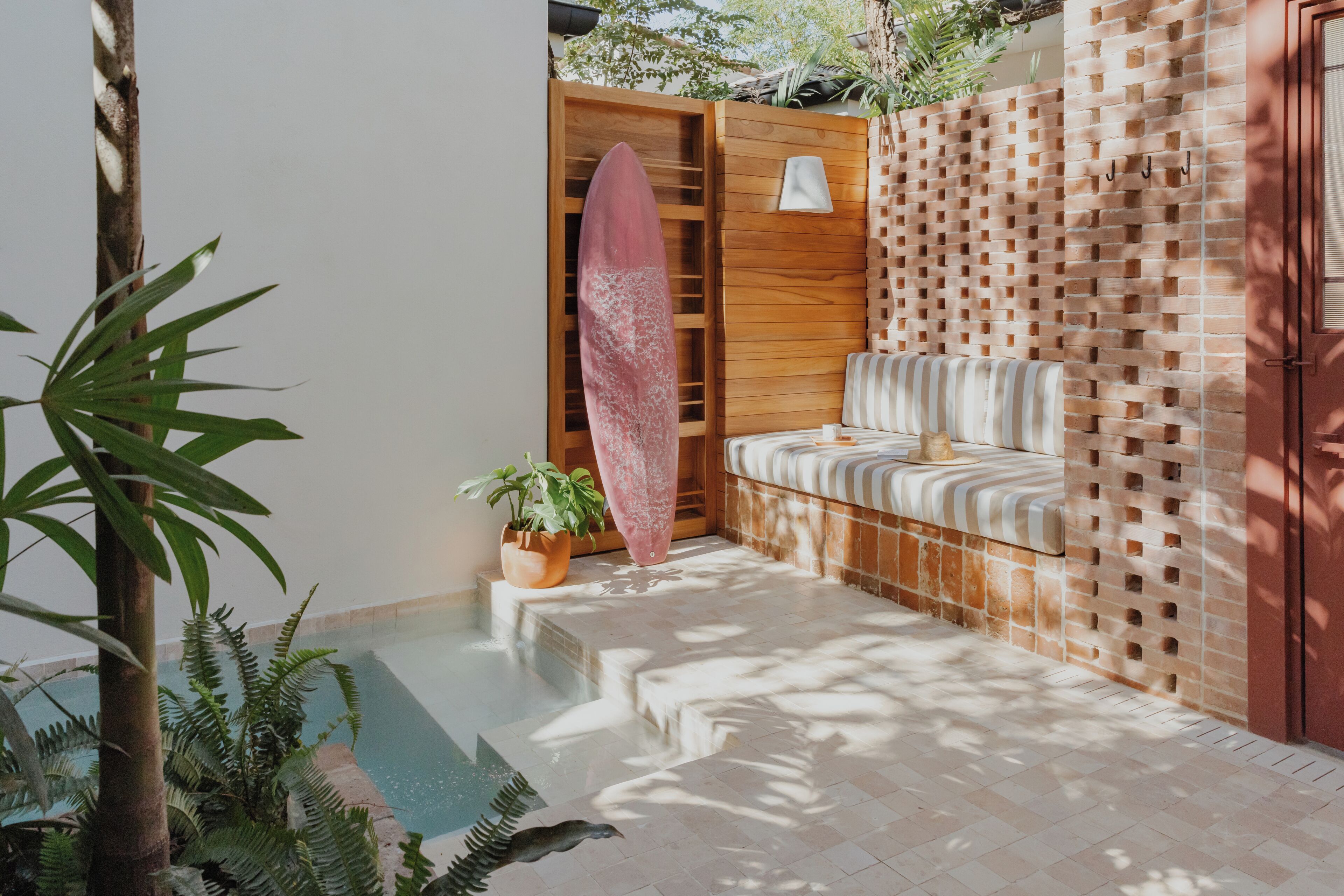 Un área de piscina con un banco de madera, una tabla de surf y plantas en macetas.
