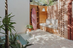 Un área de piscina con un banco de madera, una tabla de surf y plantas en macetas.