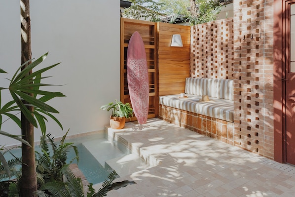 A pool area with a wooden bench, a surfboard, and potted plants. - Sendero Hotel (Nosara)
