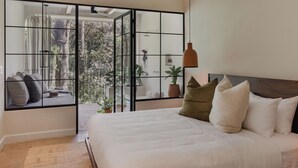 Une chambre avec un grand lit, une vue par une porte coulissante, un luminaire suspendu et une plante en pot.