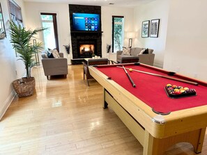 Uma sala de estar com mesa de bilhar, sofás, lareira e televisão.