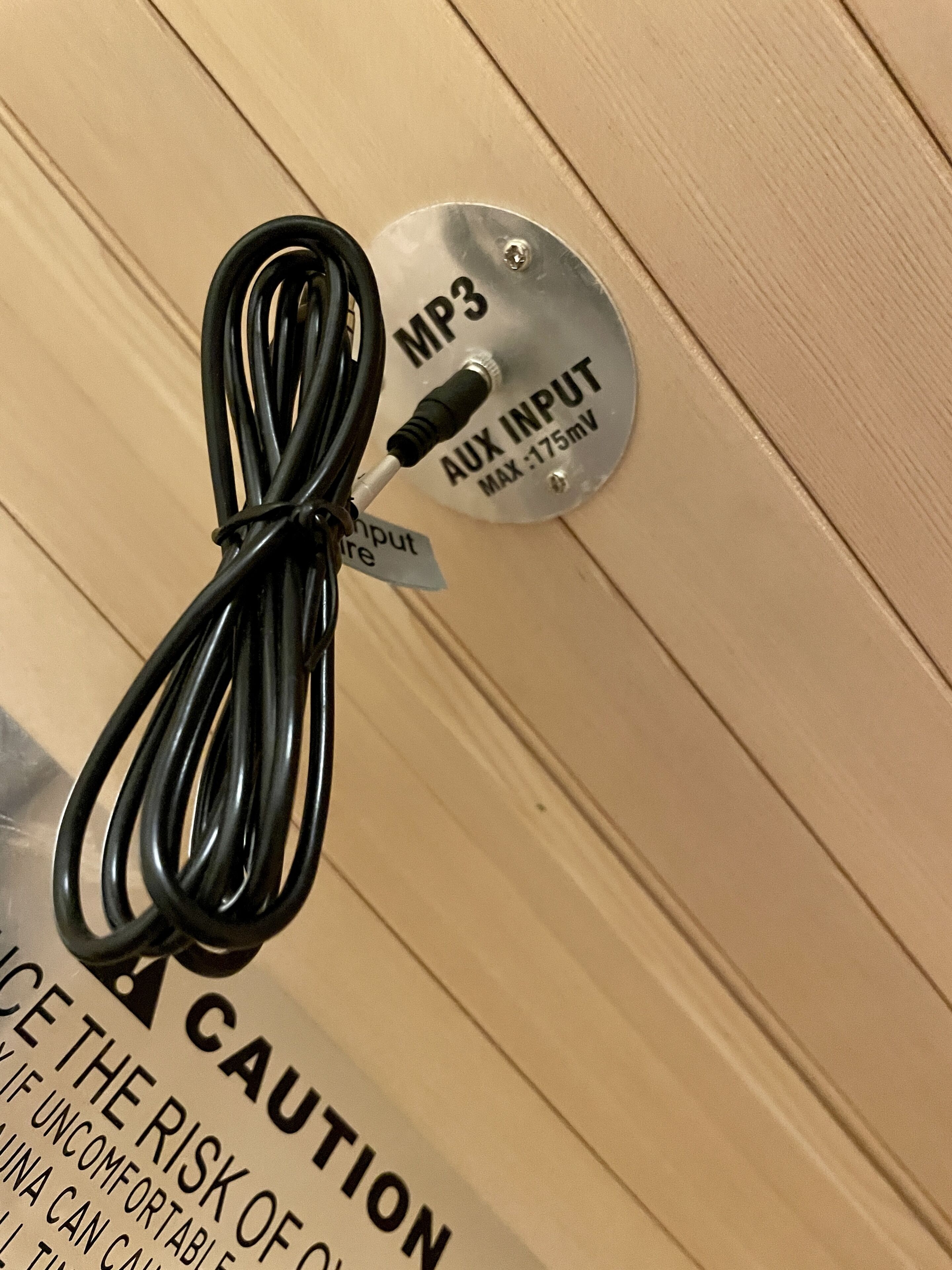 Eine Warnhinweistafel an einer Wand mit einem geschnörkelten schwarzen Kabel und einer Metallplatte mit der Aufschrift "MP3 AUX INPUT MAX: 175mV".