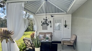 A covered patio area with a white door, a bench, a chair, and a table. - Modern studio apartment with covered outside seating area (Spring Hill)