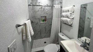 A bathroom with a shower, toilet, sink, and a mirror. - Modern studio apartment with covered outside seating area (Spring Hill)