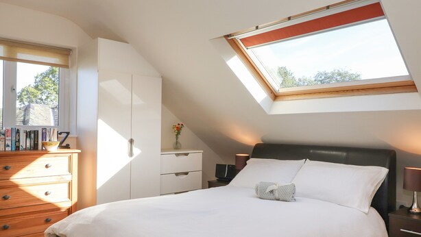 Un dormitorio con tragaluz, una cama, una mesita de noche, un aparador y una estantería.